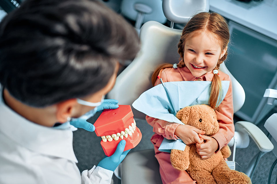 Young girl smiling during her first orthodontist visit while the clinician shows her a teeth model